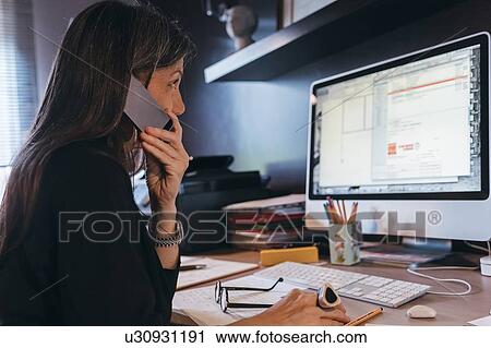 Woman using cellphone at desktop View Large Photo Image Stock Image - Woman using cellphone at desktop. Fotosearch