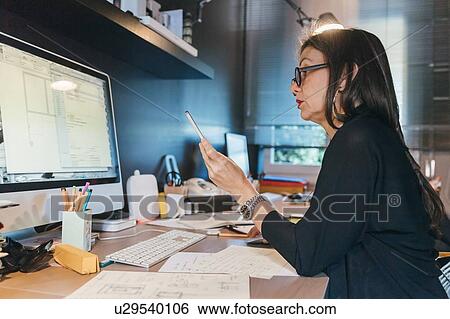 Woman using cellphone at desktop View Large Photo Image Stock Photograph - Woman using cellphone at desktop. Fotosearch