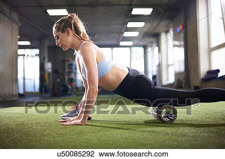 Stock Image - Woman using foam roller in gym. Fotosearch