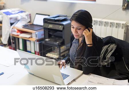 Woman using laptop and telephone in office View Large Photo Image Stock Image - Woman using laptop and telephone in office. Fotosearch