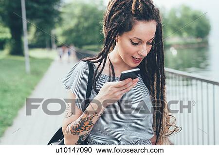 Woman using mobile phone in park View Large Photo Image Stock Image - Woman using mobile phone in park. Fotosearch