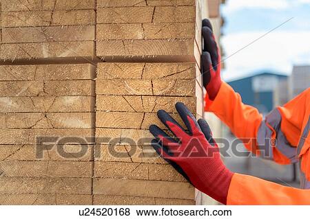 Stock Photo - Worker inspecting stacks of timber in storage at port. Fotosearch