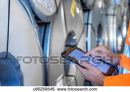 Worker using digital tablet to inspect rows of sheet steel in storage at port View Large Photo Image Stock Photograph - Worker using digital tablet to inspect rows of sheet steel in storage at port. Fotosearch