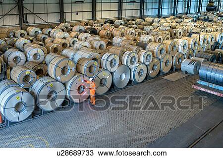Stock Image - Worker with rows of sheet steel in storage at port. Fotosearch