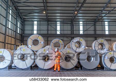 Stock Image - Worker with rows of sheet steel in storage at port. Fotosearch