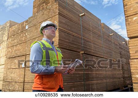 Stock Photography - Worker with stacks of timber in storage at port. Fotosearch