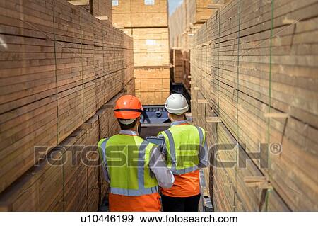 Stock Photo - Workers among stacks of timber in storage at port. Fotosearch