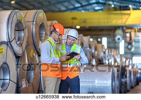 Stock Photo - Workers using digital tablet by rows of sheet steel in storage at port. Fotosearch