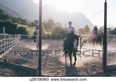 Stock Image - Young adults horse riding in rural equestrian arena, Primaluna, Trentino-Alto Adige, Italy. Fotosearch