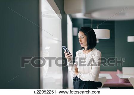 Young businesswoman in hotel looking at smartphone View Large Photo Image Stock Image - Young businesswoman in hotel looking at smartphone. Fotosearch