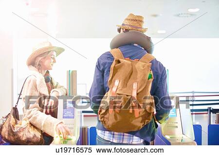 Stock Photography - Young couple at airport, carrying backpacks, walking through turnstile. Fotosearch