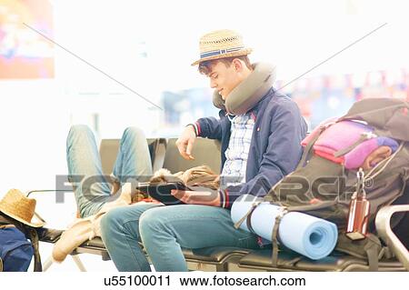 Young couple in departure lounge at airport, woman resting head on man's legs, man using digital tablet View Large Photo Image Stock Image - Young couple in departure lounge at airport, woman resting head on man's legs, man using digital tablet. Fotosearch