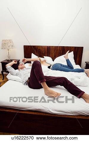 Stock Image - Young couple reclining on bed. Fotosearch
