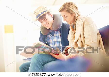 Stock Photo - Young couple sitting in airport departure lounge, looking at map, planning trip, low angle view. Fotosearch