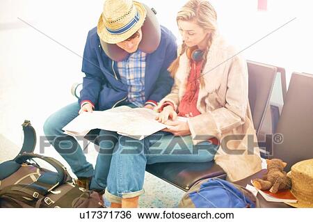 Young couple sitting in airport departure lounge, looking at map, planning trip View Large Photo Image Stock Photograph - Young couple sitting in airport departure lounge, looking at map, planning trip. Fotosearch