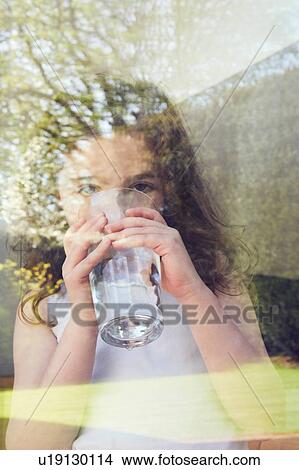 Picture - Young girl drinking water by glass window. Fotosearch