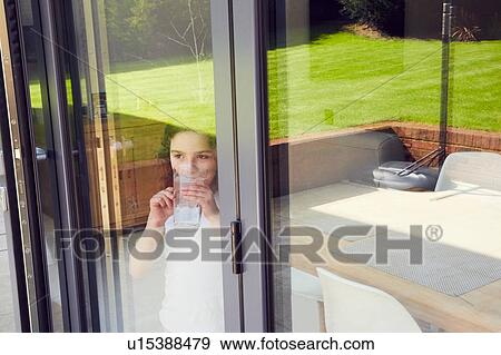 Young girl drinking water by patio door View Large Photo Image Stock Photo - Young girl drinking water by patio door. Fotosearch