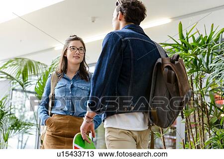 Stock Image - Young male and female university students chatting in university lobby. Fotosearch