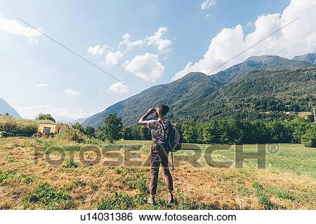 Young male hiker looking through binoculars towards mountains, Primaluna, Trentino-Alto Adige, Italy View Large Photo Image Stock Photograph - Young male hiker looking through binoculars towards mountains, Primaluna, Trentino-Alto Adige, Italy. Fotosearch