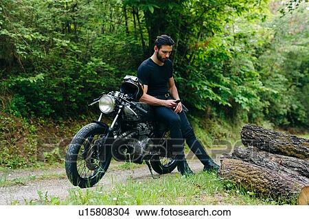 Young male motorcyclist on vintage motorcycle on rural roadside looking at smartphone, Florence, Tuscany, Italy View Large Photo Image Picture - Young male motorcyclist on vintage motorcycle on rural roadside looking at smartphone, Florence, Tuscany, Italy. Fotosearch