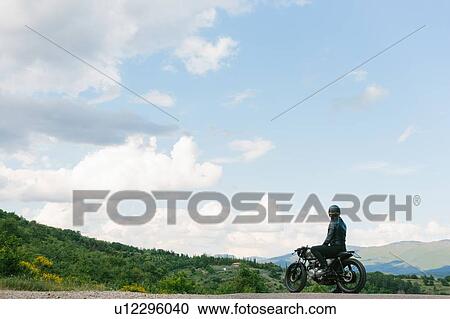 Young male motorcyclist on vintage motorcycle looking out over landscape, Florence, Tuscany, Italy View Large Photo Image Stock Image - Young male motorcyclist on vintage motorcycle looking out over landscape, Florence, Tuscany, Italy. Fotosearch