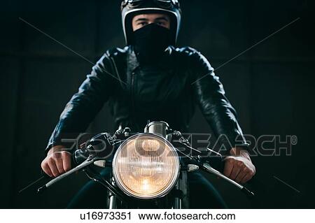 Stock Image - Young male motorcyclist on vintage motorcycle in garage, portrait. Fotosearch