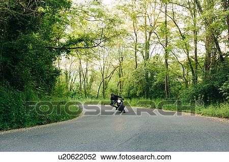 Stock Image - Young male motorcyclist on vintage motorcycle on rural road bend, Florence, Tuscany, Italy. Fotosearch