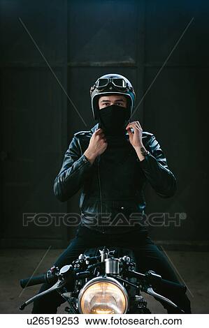 Stock Image - Young male motorcyclist on vintage motorcycle in garage, portrait. Fotosearch