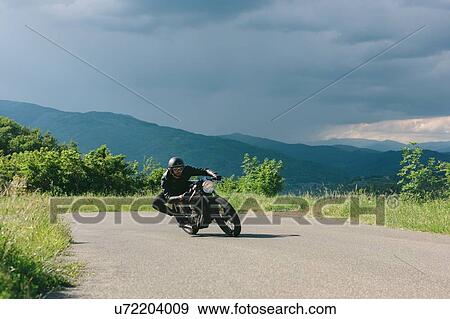 Young male motorcyclist on vintage motorcycle swerving around rural road bend, Florence, Tuscany, Italy View Large Photo Image Stock Photo - Young male motorcyclist on vintage motorcycle swerving around rural road bend, Florence, Tuscany, Italy. Fotosearch