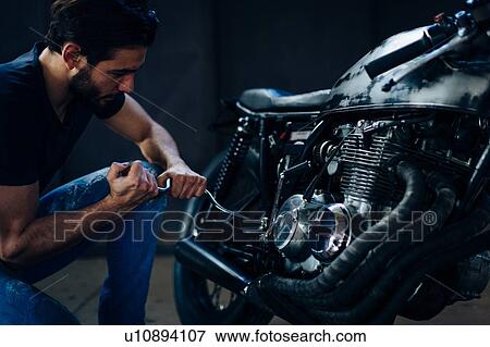 Young male motorcyclist repairing vintage motorcycle in garage View Large Photo Image Stock Photo - Young male motorcyclist repairing vintage motorcycle in garage. Fotosearch