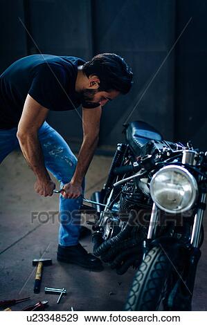 Young male motorcyclist repairing vintage motorcycle in garage View Large Photo Image Stock Photo - Young male motorcyclist repairing vintage motorcycle in garage. Fotosearch