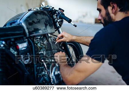 Stock Photo - Young male motorcyclist repairing vintage motorcycle outdoors. Fotosearch