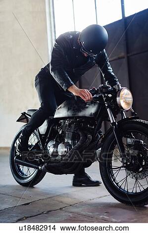 Picture - Young male motorcyclist revving vintage motorcycle in garage. Fotosearch