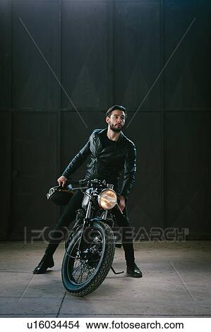 Young male motorcyclist straddling vintage motorcycle in empty warehouse View Large Photo Image Picture - Young male motorcyclist straddling vintage motorcycle in empty warehouse. Fotosearch
