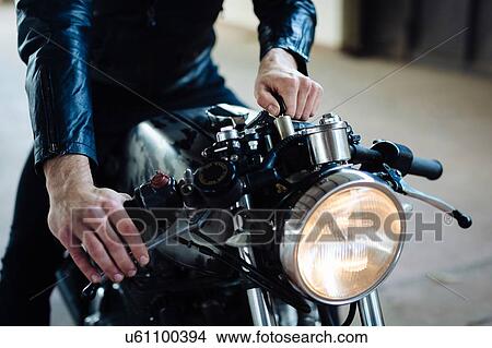 Young male motorcyclist straddling vintage motorcycle in garage, cropped View Large Photo Image Picture - Young male motorcyclist straddling vintage motorcycle in garage, cropped. Fotosearch