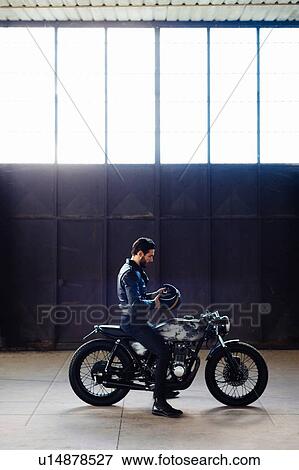 Young male motorcyclist straddling vintage motorcycle in empty warehouse, full length View Large Photo Image Stock Photo - Young male motorcyclist straddling vintage motorcycle in empty warehouse, full length. Fotosearch