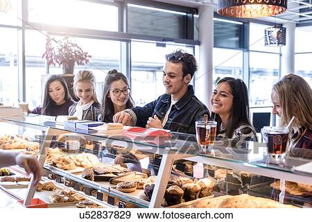 Stock Photo - Young male student and female friends queueing at cafe counter. Fotosearch