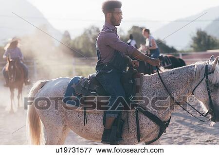 Stock Photo - Young man and friends horse riding in rural equestrian arena, Primaluna, Trentino-Alto Adige, Italy. Fotosearch