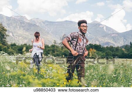 Stock Image - Young man and woman racing through wildflower meadow, Primaluna, Trentino-Alto Adige, Italy. Fotosearch