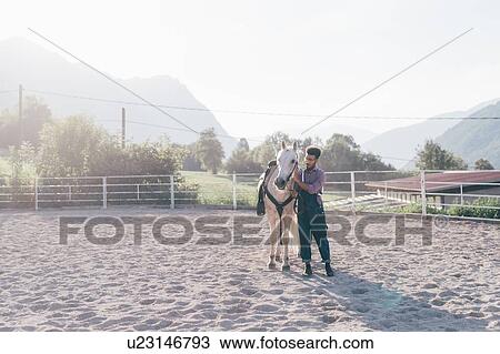 Stock Image - Young man bonding with horse in rural equestrian arena, Primaluna, Trentino-Alto Adige, Italy. Fotosearch