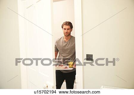 Picture - Young man carrying breakfast tray into bedroom. Fotosearch