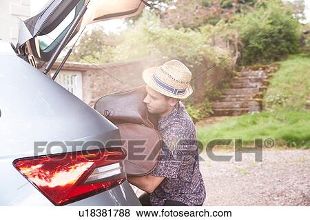 Young man in trilby removing luggage from car boot outside hotel View Large Photo Image Stock Photo - Young man in trilby removing luggage from car boot outside hotel. Fotosearch
