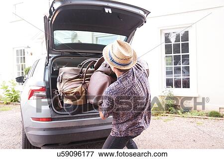 Young man in trilby removing luggage from car boot outside hotel, rear view View Large Photo Image Stock Photo - Young man in trilby removing luggage from car boot outside hotel, rear view. Fotosearch