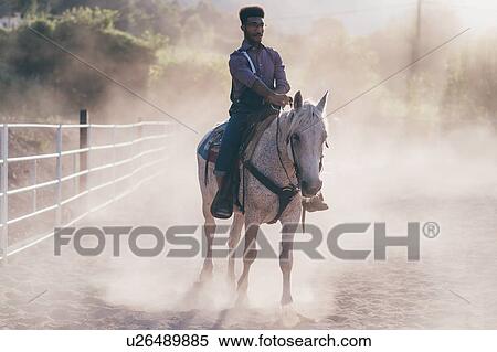 Stock Photography - Young man on horse in dusty equestrian arena, Primaluna, Trentino-Alto Adige, Italy. Fotosearch
