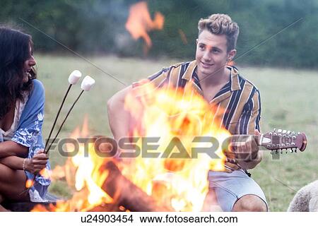 Picture - Young man playing guitar at bonfire party in park. Fotosearch