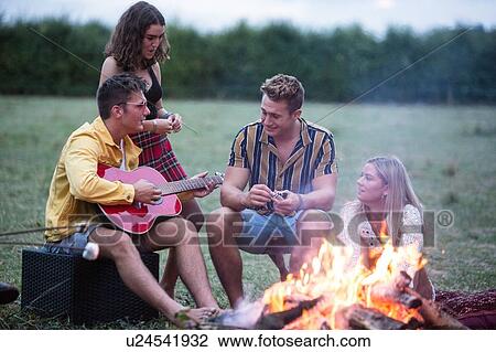 Stock Image - Young man playing guitar at bonfire party in park. Fotosearch