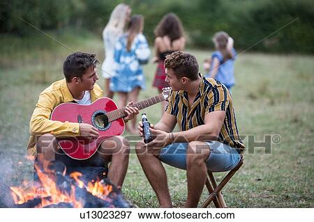 Young man playing guitar at bonfire party in park View Large Photo Image Stock Photo - Young man playing guitar at bonfire party in park. Fotosearch