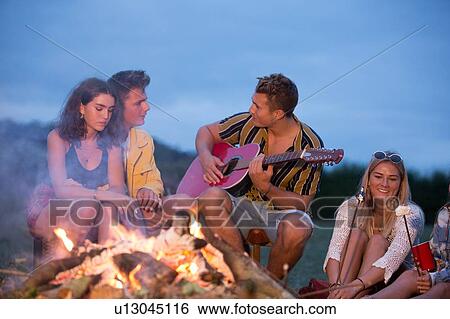 Stock Photograph - Young man playing guitar at bonfire party in park. Fotosearch