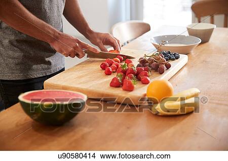 Young man slicing fresh fruit at kitchen table, mid section View Large Photo Image Picture - Young man slicing fresh fruit at kitchen table, mid section. Fotosearch
