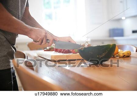 Young man slicing fresh fruit at kitchen table, mid section View Large Photo Image Stock Image - Young man slicing fresh fruit at kitchen table, mid section. Fotosearch